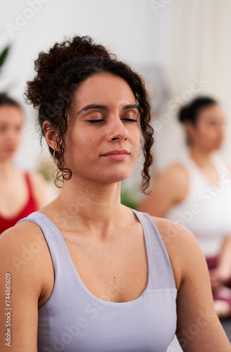 Vertical close up of a young female instructor in yoga lessons, sitting in Sukhasana, meditating inside studio. Wellness and mental healthcare help.