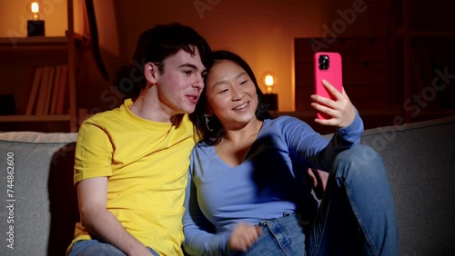 Teenager couple having video call on phone at night. Woman sitting on sofa with her boyfriend.