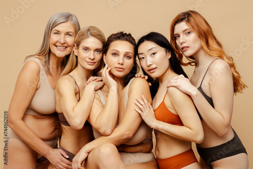Group portrait beautiful smiling multiethnic women hugging, wearing sexy lingerie isolated on beige background. Attractive stylish fashion models with perfect makeup looking at camera. Natural beauty