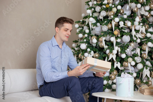  Young handsome man sitting in living room and holding Christmas gift