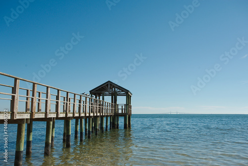View out Bay Vista Park  with a pier on the left  with leading lines of wood pier  towards Tampa Bay and the Skyway Bridge on a sunny afternoon in St. Petersburg, FL. Sunlight and reflections in water © Del Harper