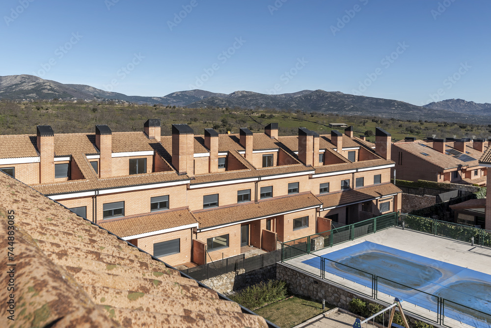 An urbanization of semi-detached single-family homes of various heights next to a mountain range with common areas with swimming pools and children's play areas