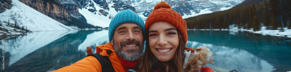 Couple travel selfie banner landscape happy hikers in winter alps lake view. Asian woman, Caucasian man using mobile phone taking selfie by the lake in the mountains Couple travel selfie banner landscape happy hikers in winter alps lake view. Asian woman, Caucasian man using mobile phone taking selfie by the lake in the mountains