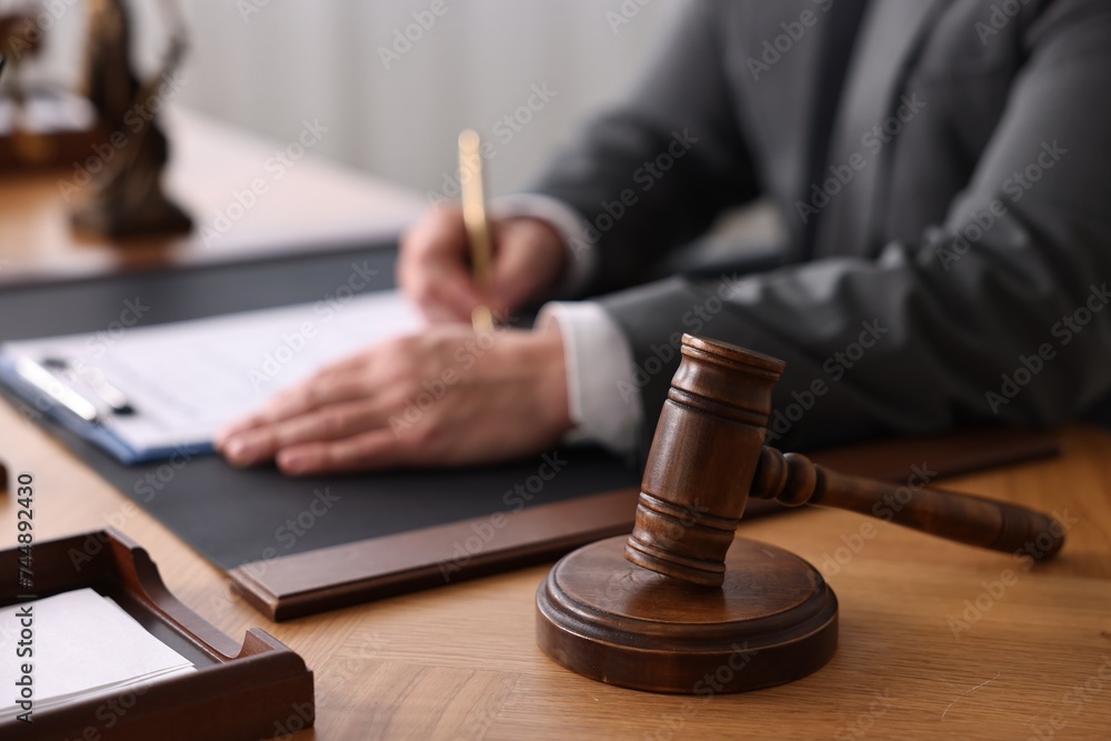 Notary writing notes at wooden table in office, focus on gavel Notary writing notes at wooden table in office, focus on gavel