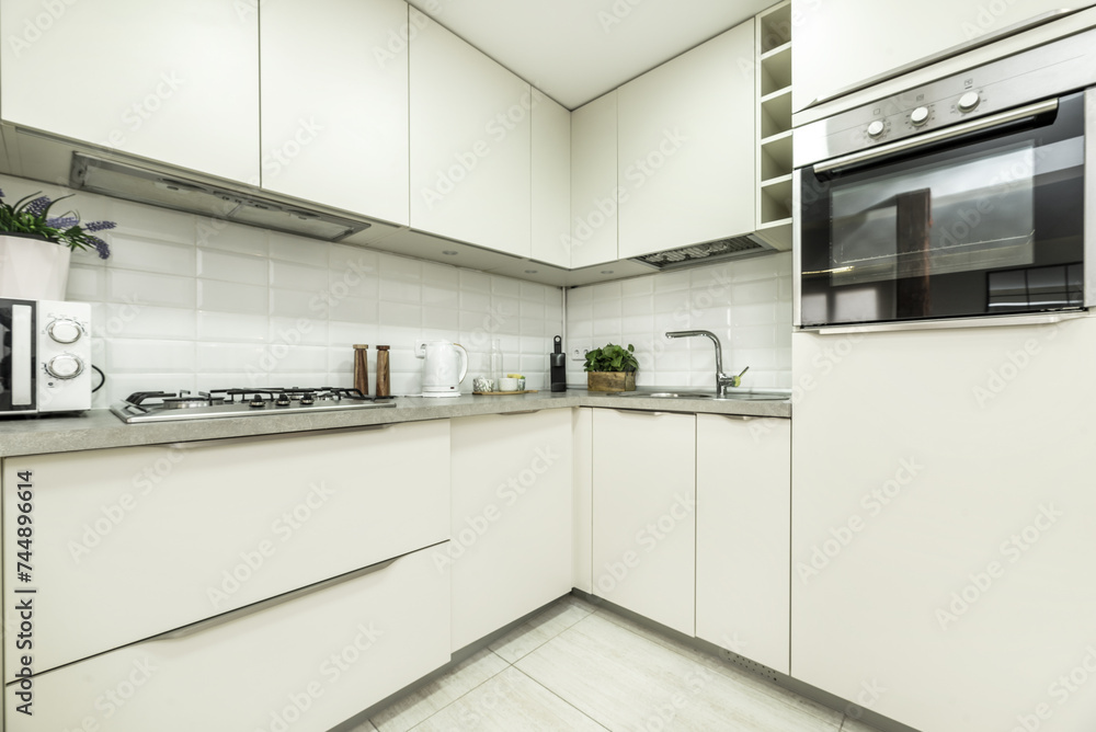 Kitchen corner furnished with white cabinets, gray countertop, integrated extractor hood, column with stainless steel oven Kitchen corner furnished with white cabinets, gray countertop, integrated extractor hood, column with stainless steel oven