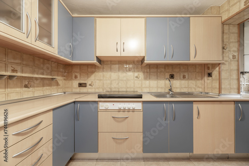 Frontal image of a kitchen furnished with light wood furniture combined with pale blue, aluminum handles, a wood-colored countertop and integrated white appliances