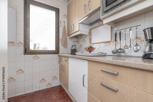 Small kitchen furnished with white furniture combined with light wood  aluminum handles  pink copy granite countertop and integrated appliances and a single-leaf window on the wall