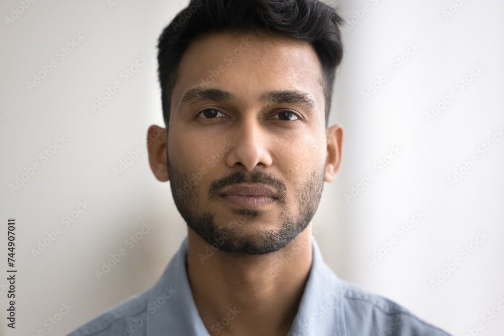 Close up of unsmiling Indian bearded guy standing indoor staring at camera. Man having attractive appearance, looks confident and serious. Millennial generation person, businessman head shot portrait Close up of unsmiling Indian bearded guy standing indoor staring at camera. Man having attractive appearance, looks confident and serious. Millennial generation person, businessman head shot portrait