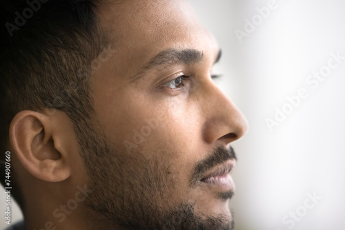 Close up photo of young thoughtful Indian man looking into distance, deep in thoughts, ponder, visualize, recollect memories or past staring straight, side profile face view. Male appearance, beauty