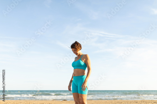 A woman rests after performing Pilates exercises on the beach, facing the sea