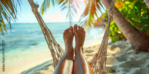 Close-up of bare feet in a hammock on a tropical beach with palm trees. photo