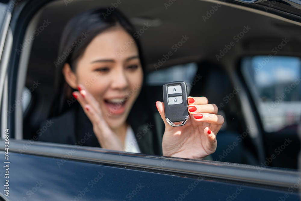 Young beautiful asian business women in suit getting new car showing car key. she very happy and excited in hand holding car key. Smiling female driving vehicle on the road city on a bright day