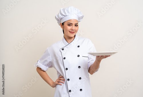 Obraz na plátně Smiling Young beautiful asian woman chef in uniform holding empty plate delicious dish menu good taste on isolated