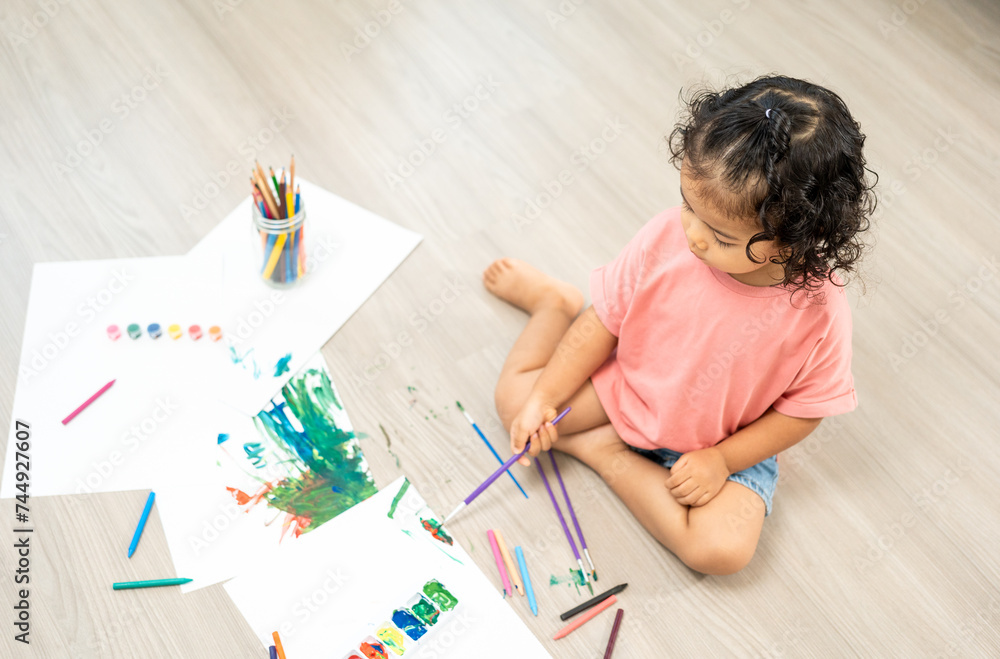 Happy moment little cute girl creating and water color painting activity with paint brushes on frame canvas at living room. Kids activity. Child physical, Emotional, Cognitive development concept. Happy moment little cute girl creating and water color painting activity with paint brushes on frame canvas at living room. Kids activity. Child physical, Emotional, Cognitive development concept.
