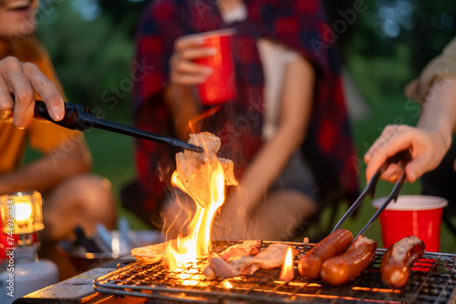Cheers! Group of asian people friend party camping in nature making barbecue grilled. Hangout party outdoor in campsite nature forest background on holiday weekend vacation in the evening.