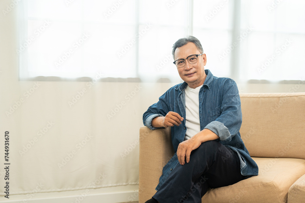 Handsome asian mature old man sitting on sofa couch in living room at home. Happy Portrait of cheerful smiling senior asian man relax in the house. Mature People and lifestyle Handsome asian mature old man sitting on sofa couch in living room at home. Happy Portrait of cheerful smiling senior asian man relax in the house. Mature People and lifestyle