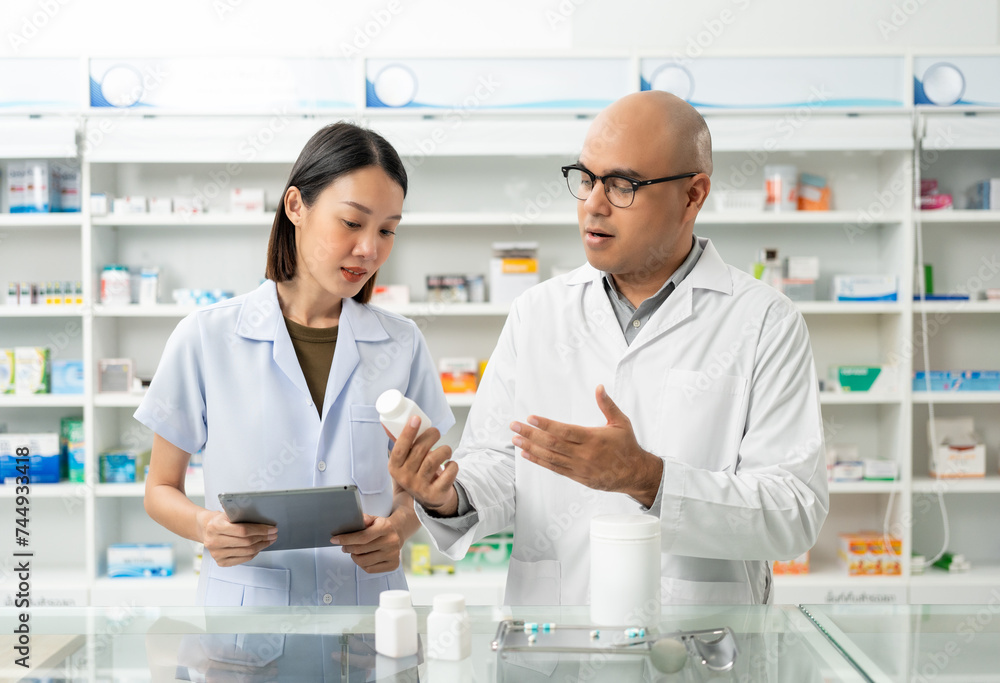 Two asian man and woman professional Pharmacist colleagues working at drugstore pharmacy. Asking the questions of medication standing near pharmacy shelves counter with medicines