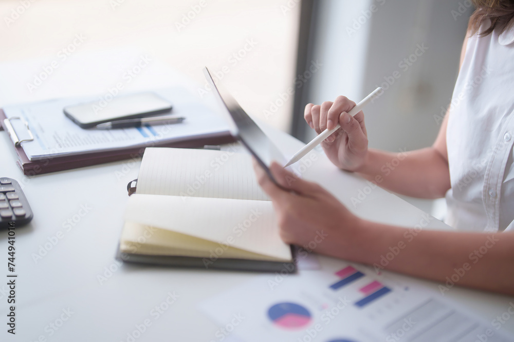 Fototapeta premium Asian businesswomen reading marketing business report on digital tablet and finance document of new business to taking notes while analyze investment and market stock of new startup in outside office