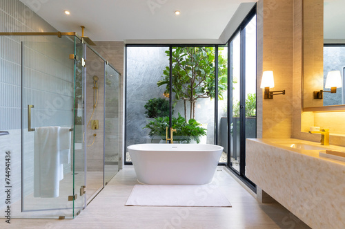 Modern luxury bathroom with marble floor and wall, Rooms have large windows and white bathtub.