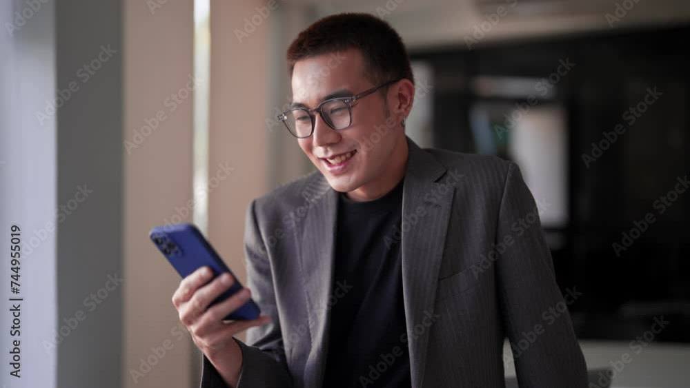 Young Asian businessman typing messages or reading news on his smartphone at his work desk Young Asian businessman typing messages or reading news on his smartphone at his work desk
