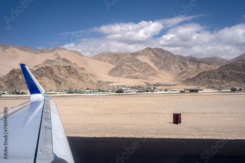 A shot from airplane window  visible plane wings. Dry Mountains with runway in the foreground and mountains in the back with clear blue sky and clouds