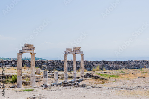 Ancient stone columns standing tall amidst ruins under a clear blue sky, in Epesus Turkiye