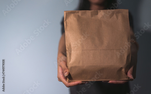 Close-up of unrecognizable person presenting a plain brown paper bag, potential for branding..