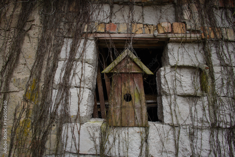 An old wooden birdhouse in a window of a crumbling building An old wooden birdhouse in a window of a crumbling building