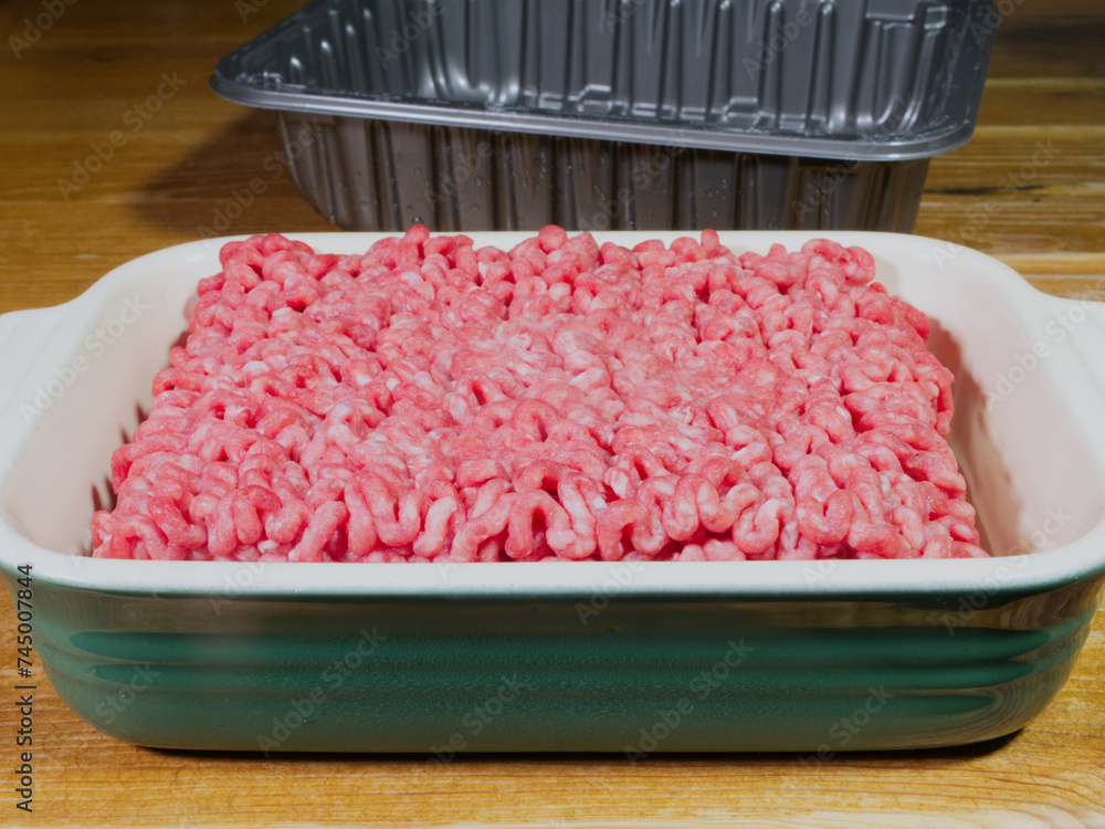 Closeup of fresh, raw minced beef steak meat, just taken out of a plastic retail tray, and resting in a ceramic dish before cooking. Closeup of fresh, raw minced beef steak meat, just taken out of a plastic retail tray, and resting in a ceramic dish before cooking.