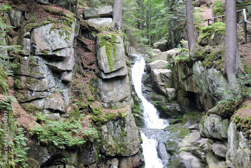Podgórna Waterfall in the Polish part of the Karkonosze Mountains falling from a steep rocky granite wall, cracked granite walls covered with green moss in the forest in the mountains in Poland