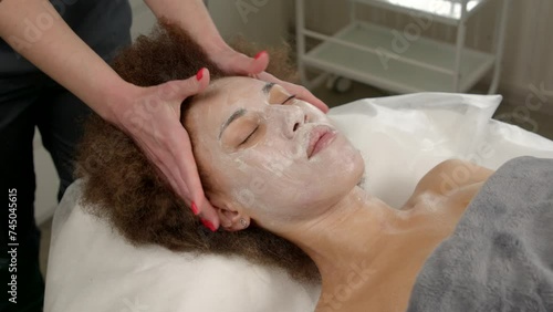 Skillful female masseuse doing beauty beauty and spa procedure, giving scalp massage to relaxed pretty African American woman, improving blood circulation and hair growth stimulation indoors. photo
