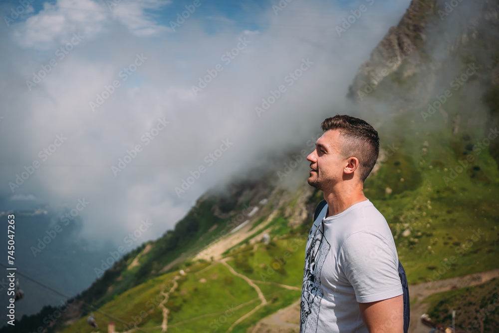 A man in light clothes against the background of mountains covered with vegetation. Hiking high in the mountains in summer, there is snow A man in light clothes against the background of mountains covered with vegetation. Hiking high in the mountains in summer, there is snow