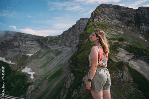 A woman the background of mountains covered with vegetation. Hiking high in the mountains in summer, there is snow