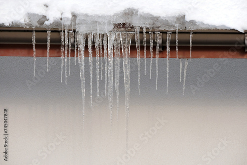 Shiny icicles hanging from the roof of the house, sunny weather, snow on the roof © E-lona