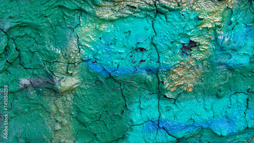 A very roughly plastered surface of an old concrete wall is painted in a combination of green, blue and gold