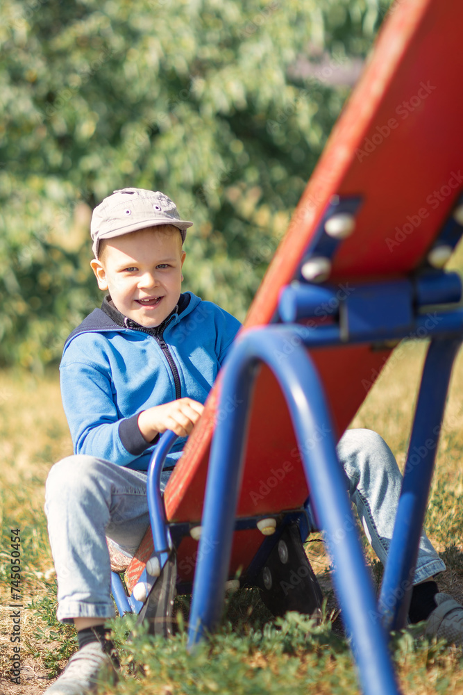 A cute boy in a blue sweater swings on a red playground.
