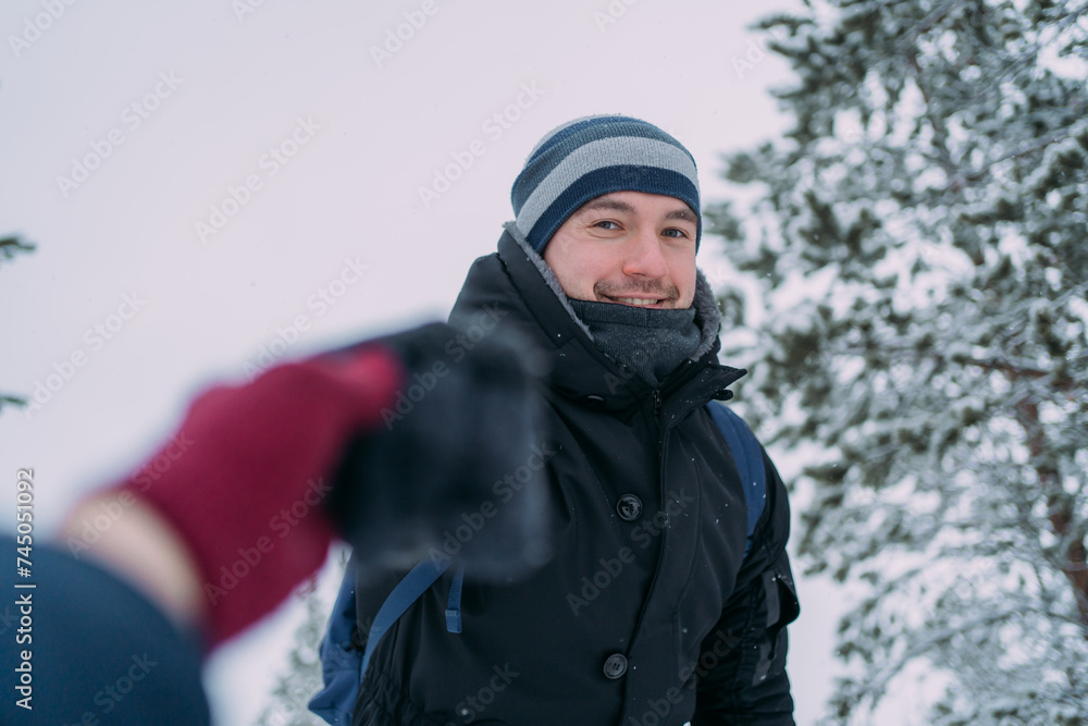 The man holds out his hand to the woman, helping her to climb up. There is only a smiling man and a woman's hand in a burgundy glove in the frame. A man in winter clothes