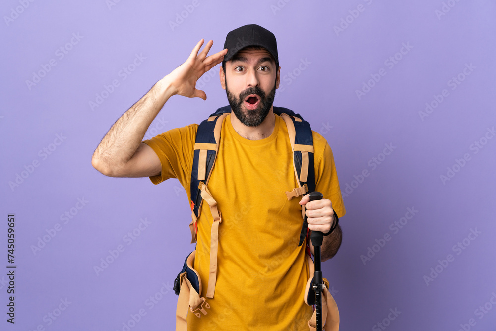 Caucasian handsome man with backpack and trekking poles over isolated background with surprise expression Caucasian handsome man with backpack and trekking poles over isolated background with surprise expression