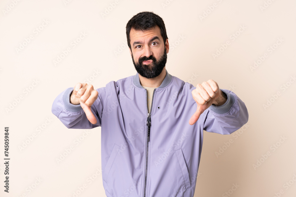 Caucasian man with beard wearing a jacket over isolated background showing thumb down with two hands Caucasian man with beard wearing a jacket over isolated background showing thumb down with two hands
