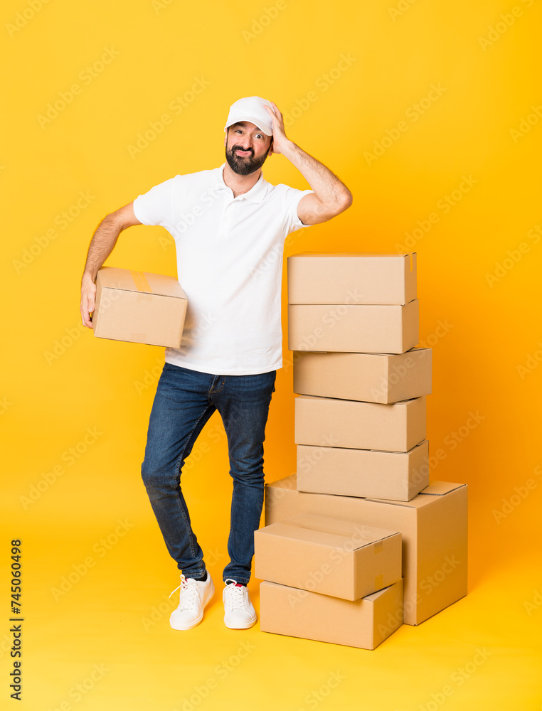 Full-length shot of delivery man among boxes over isolated yellow background with an expression of frustration and not understanding Full-length shot of delivery man among boxes over isolated yellow background with an expression of frustration and not understanding