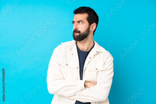 Young handsome man with white corduroy jacket over isolated blue background with confuse face expression