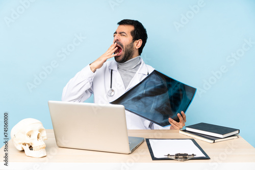 Professional traumatologist in workplace yawning and covering wide open mouth with hand photo