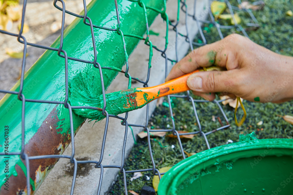 Obraz premium Cropped hand of man painting green color on chainlink fence