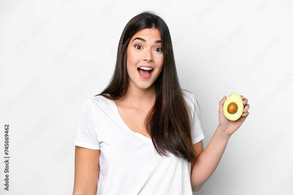 Young Brazilian woman holding an avocado isolated on white background with surprise and shocked facial expression Young Brazilian woman holding an avocado isolated on white background with surprise and shocked facial expression
