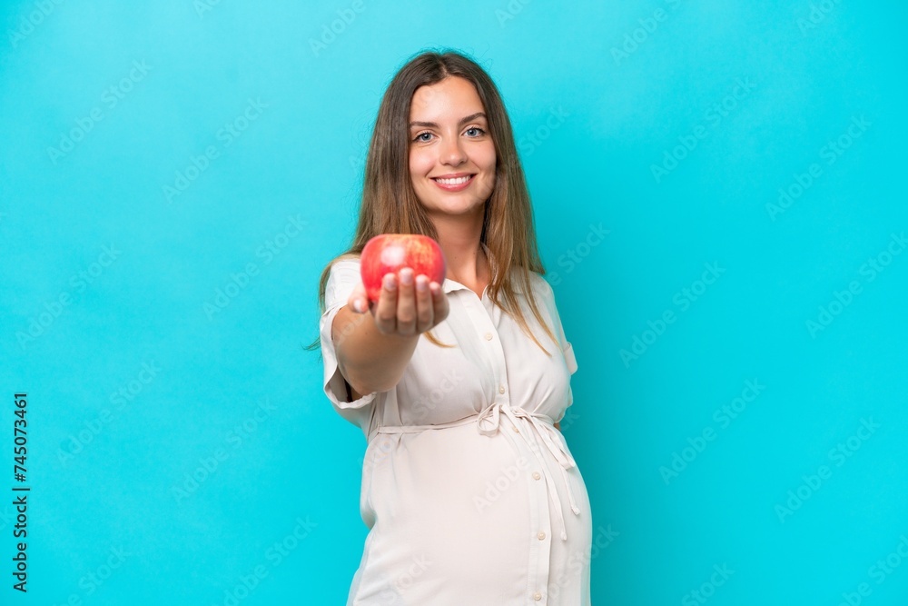 Young caucasian woman isolated on blue background pregnant and holding an apple Young caucasian woman isolated on blue background pregnant and holding an apple