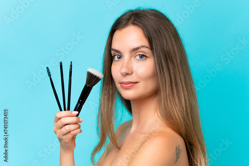 Young caucasian woman isolated on blue background holding makeup brush