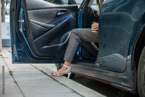 In a city setting a businesswoman in a stylish suit sits in a luxury car. Her slender leg clad in high heels gracefully opens door showcasing the blend of modern transportation and corporate glamour. photo