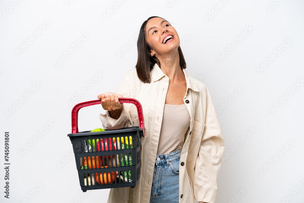 Young woman holding a shopping basket full of food isolated on white background laughing Young woman holding a shopping basket full of food isolated on white background laughing