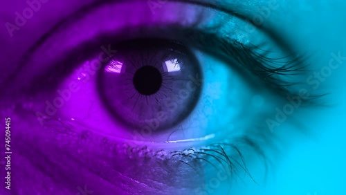 Close up shot of macro eye opening and blinking in Pink-blue-green color light. Female pink eye in neon lights. Macro look of the human eye.  photo