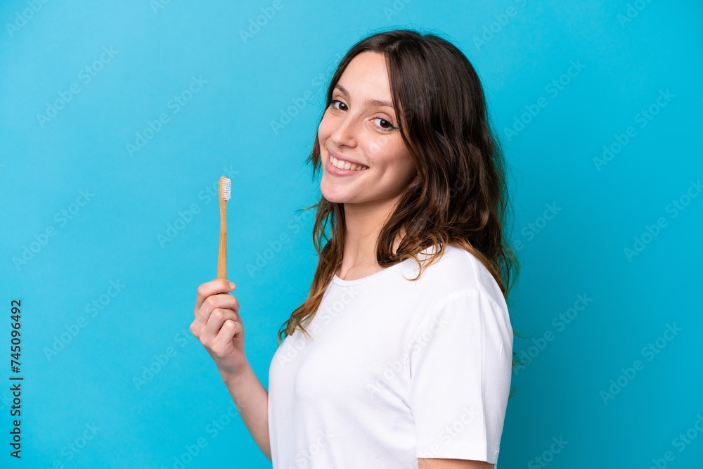Young caucasian woman brushing teeth isolated on blue background smiling a lot Young caucasian woman brushing teeth isolated on blue background smiling a lot